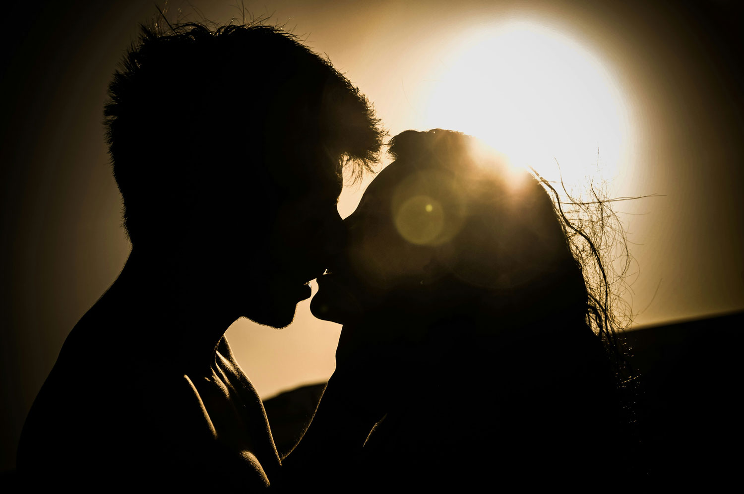 man and woman kissing at sunset